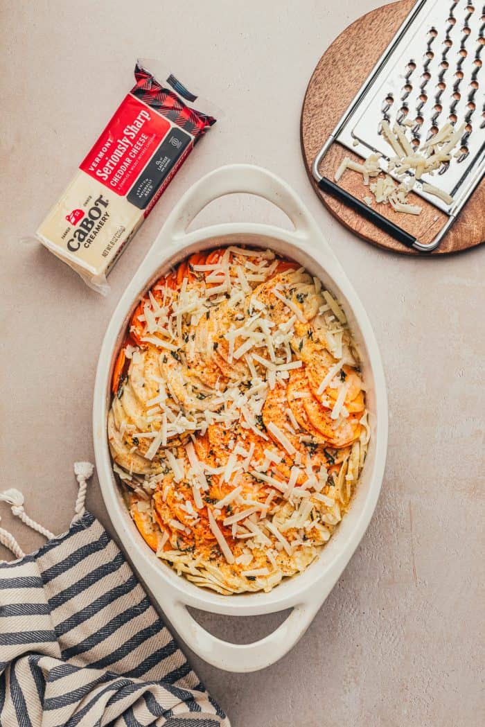 Shredded cheddar cheese over sliced root vegetables in a white baking dish.