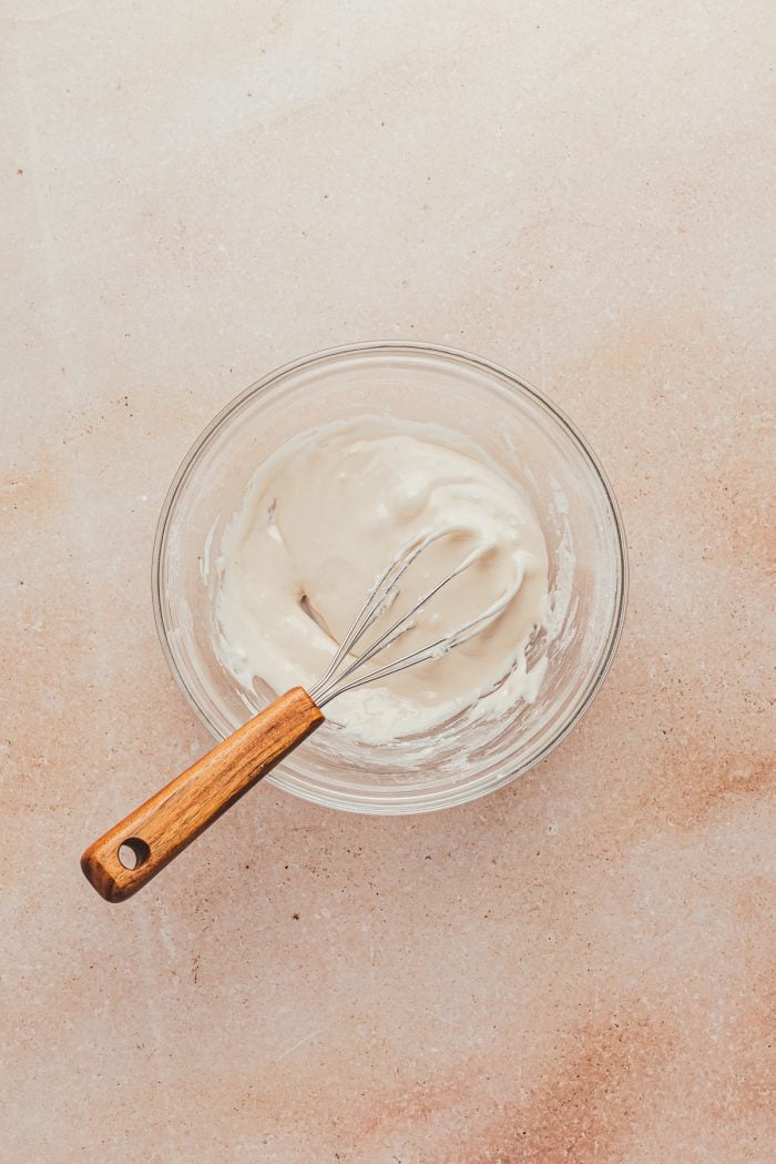 A glass bowl with icing and a whisk.