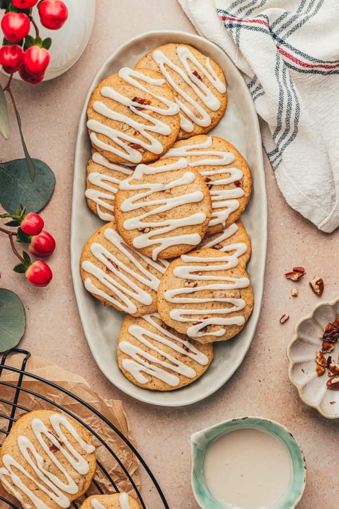 Glazed spice drop cookies with nuts on a platter with cookies in the background on a cooling rack. 