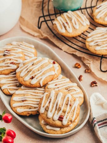 Glazed spice drop cookies with nuts on a platter with cookies in the background on a cooling rack.