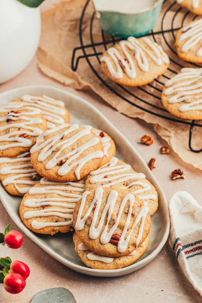 Glazed spice drop cookies with nuts on a platter with cookies in the background on a cooling rack. 