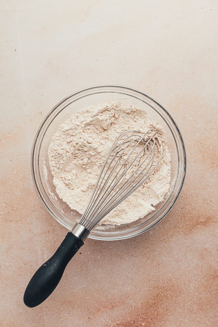 A glass bowl with flour and a whisk.