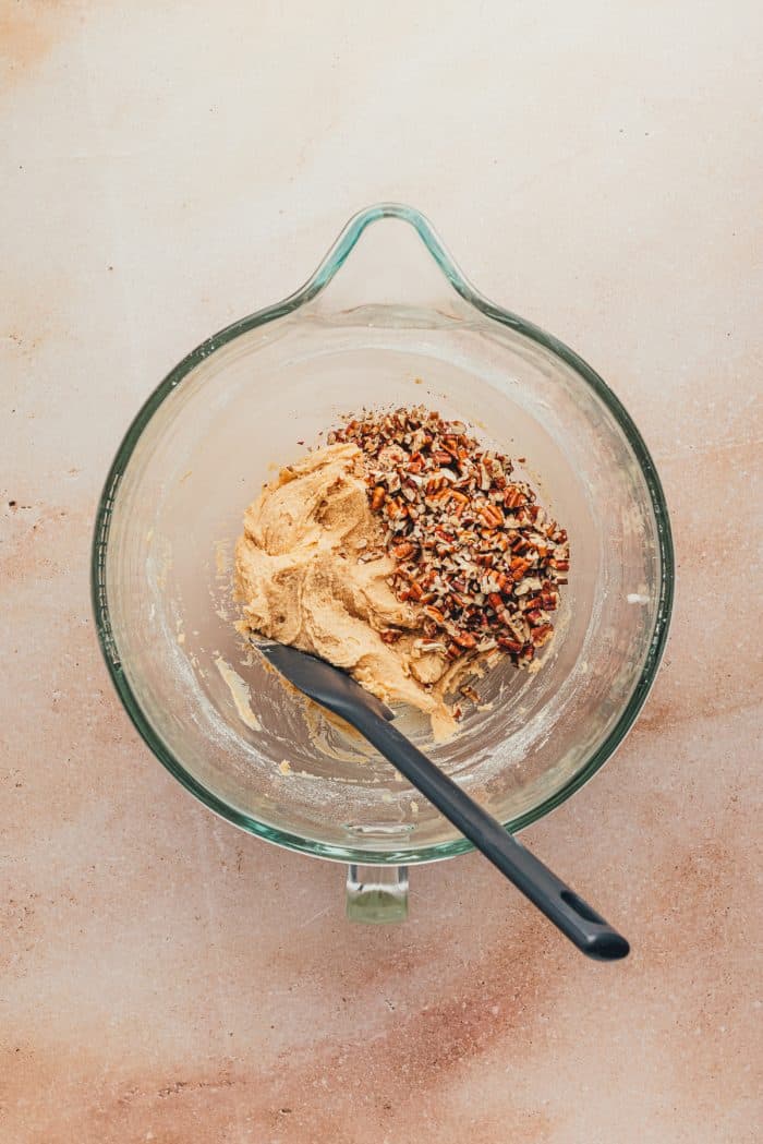 A bowl with raw cookie dough and nuts with a spatula.