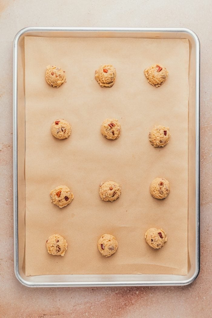 A cookie tray with parchment paper and unbaked drop cookies.