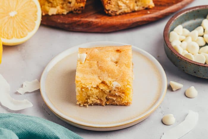 A lemon blondie on a small plate with a bowl of white chocolate chips.