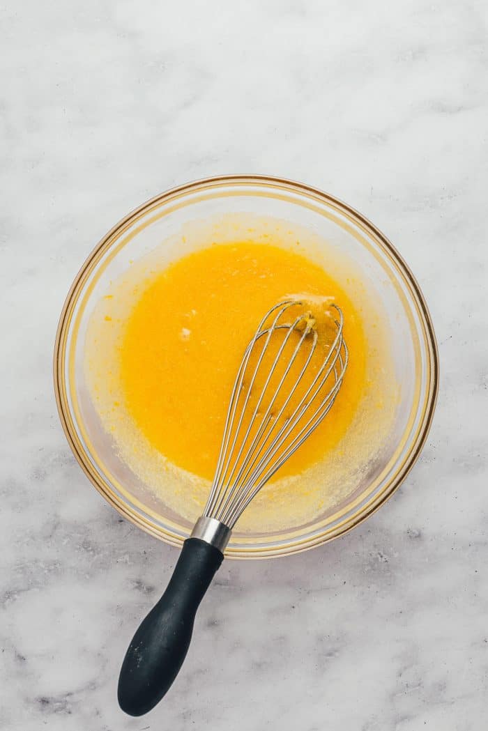 A glass bowl with an egg mixture and a whisk.