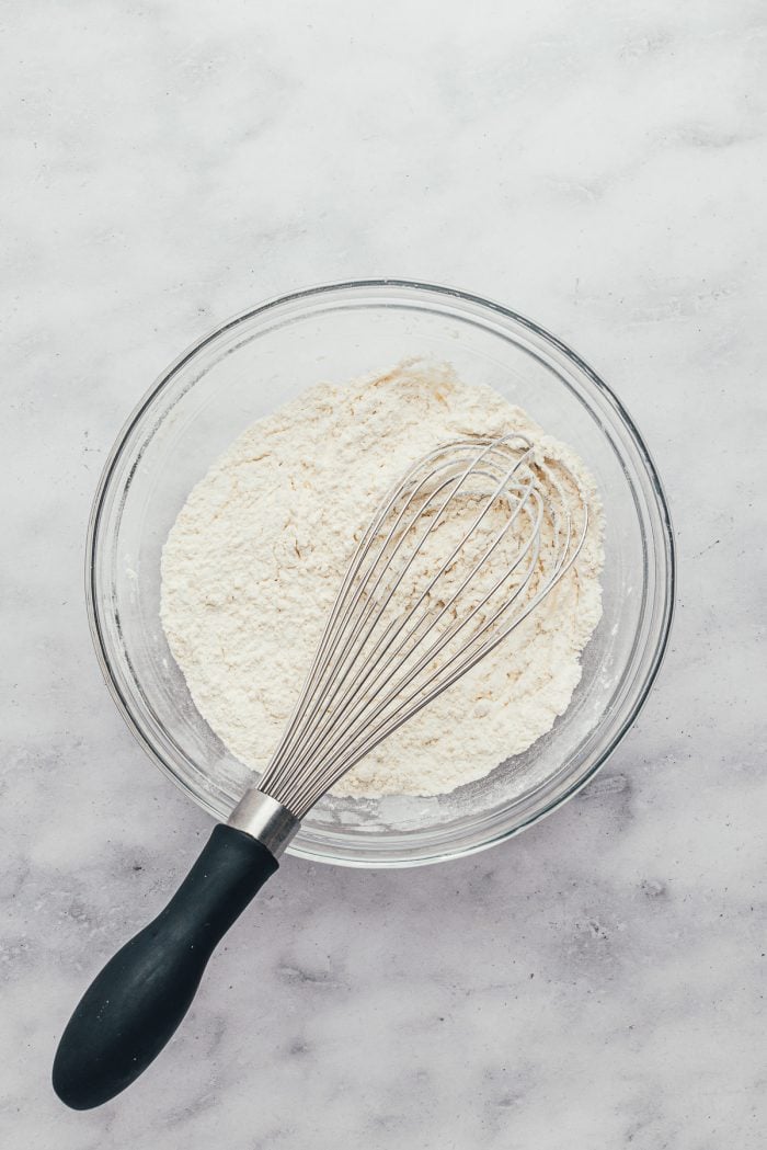 A glass bowl with flour and a whisk.