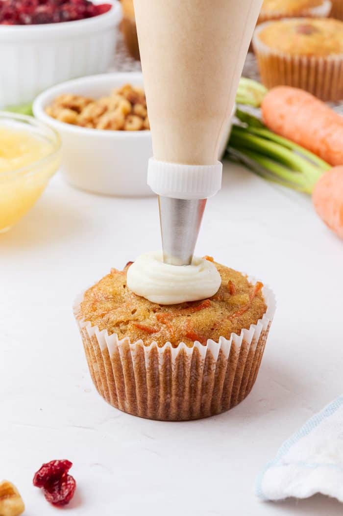 A carrot cake cupcake being topped with frosting.