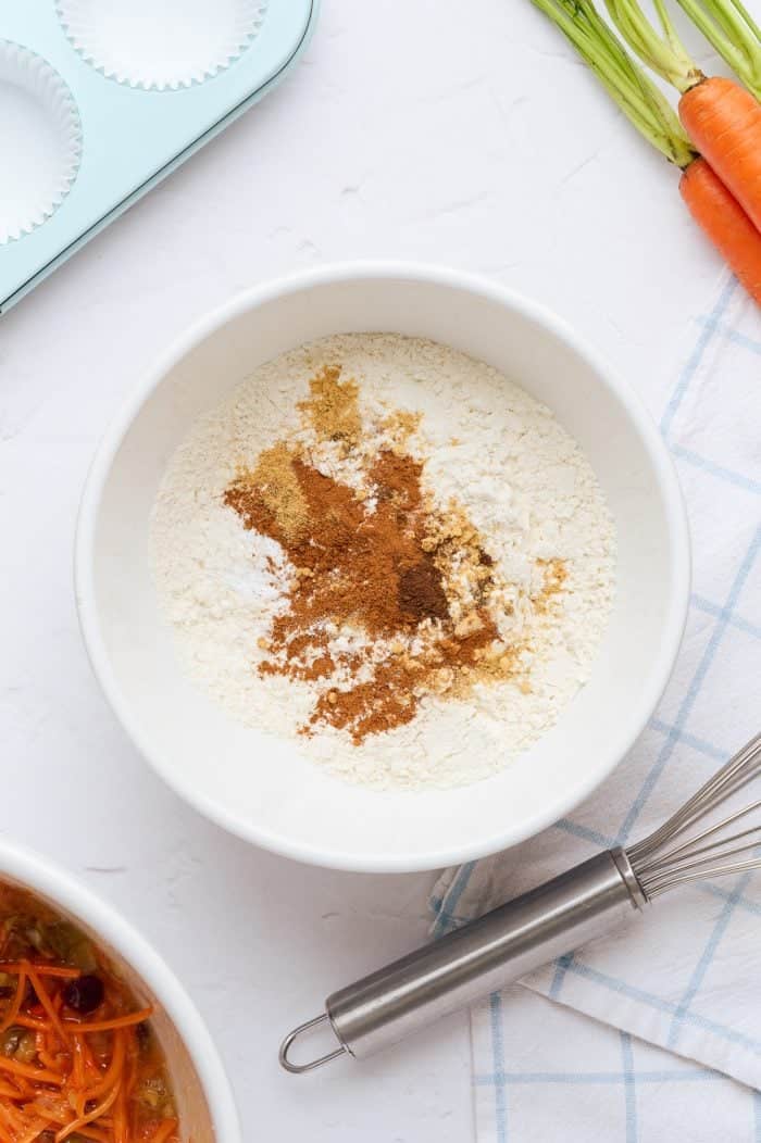 A white mixing bowl with the dry ingredients needed to make carrot cake cupcakes.