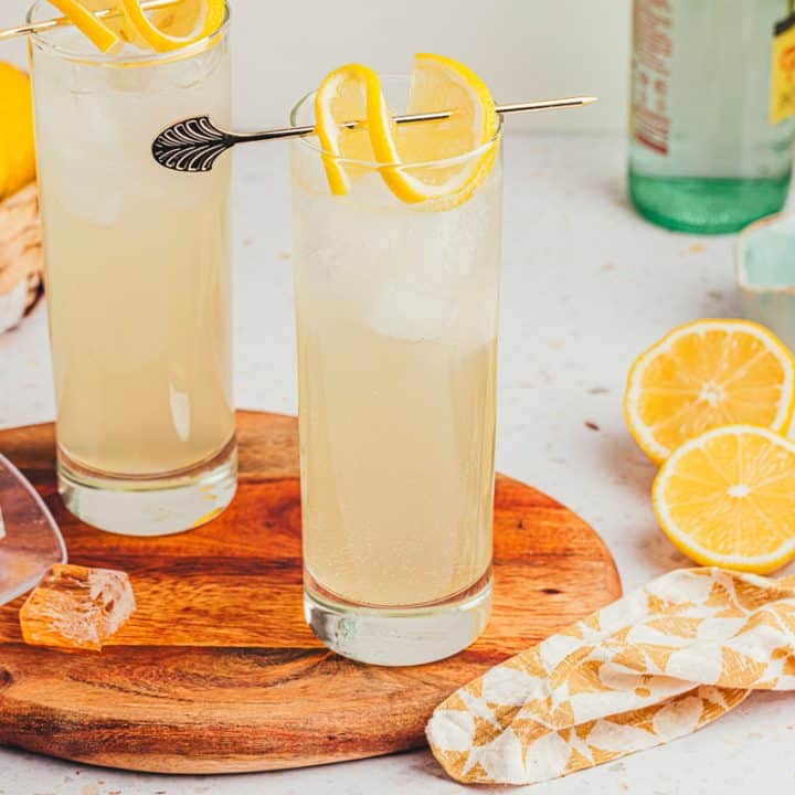 An image of two tall glasses with lemon elderflower mocktail s garnished with lemon slices on a wooden board.