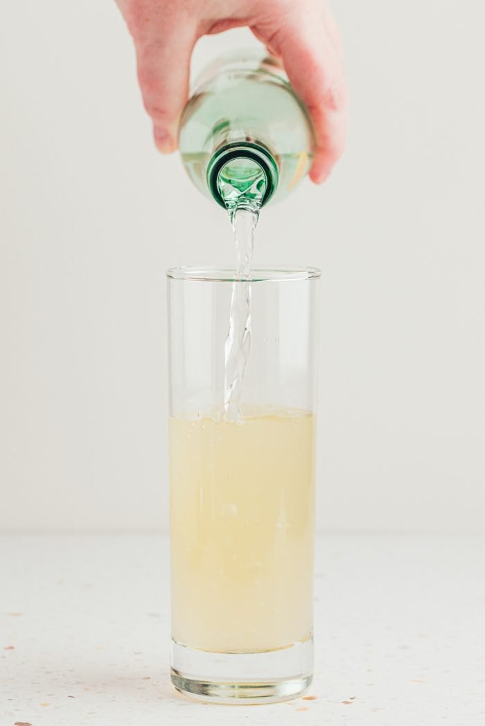 A tall glass with sparkling water being added to it.