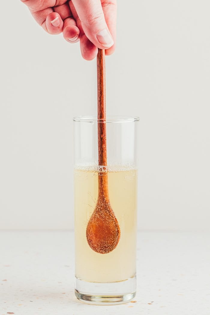 A tall glass with a wooden spoon stirring the drink.