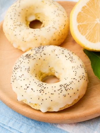 Two lemon poppyseed donuts on a wooden tray.