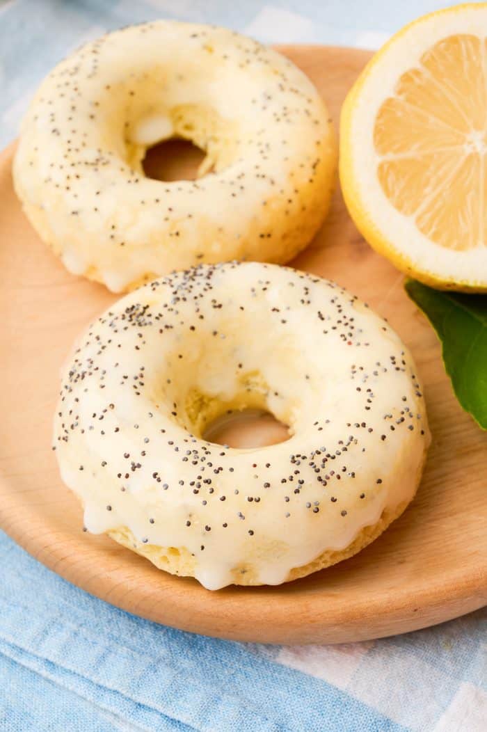 Two lemon poppyseed donuts on a wooden tray.