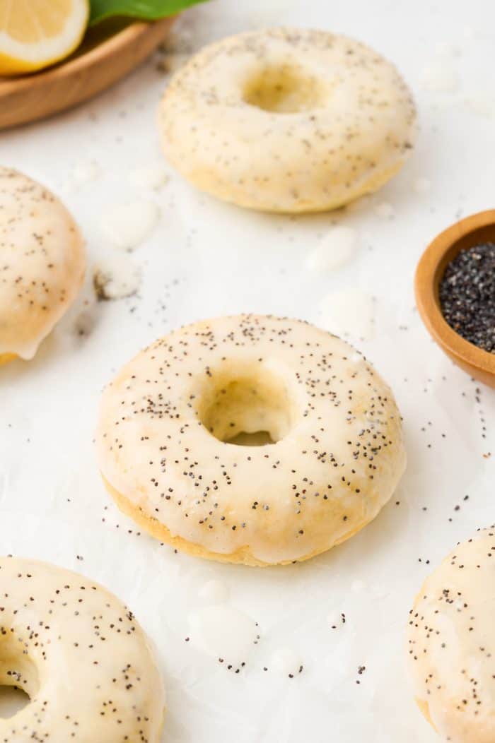 Various lemon poppyseed donuts on a counter with a bowl of poppyseeds.