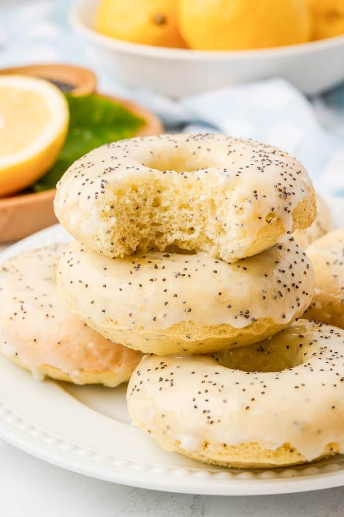 Various lemon donuts stacked on a plate and one has a bite taken out of it.