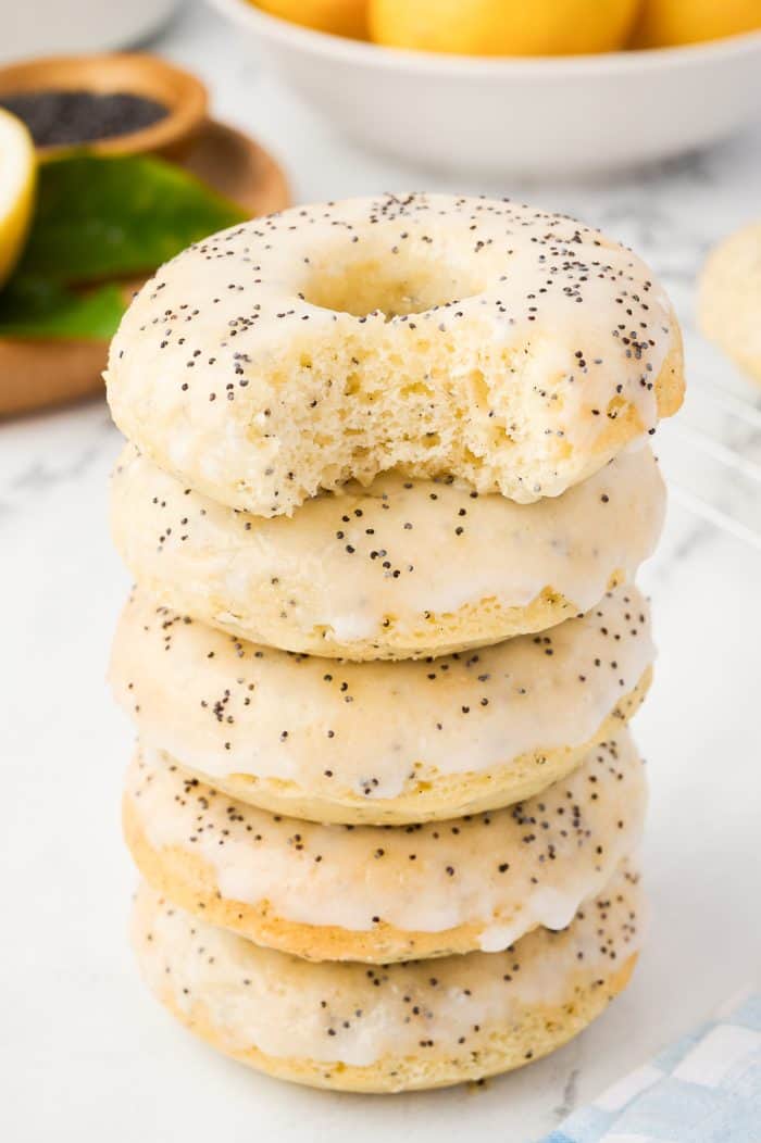 Various lemon donuts stacked on a counter and one has a bite taken out of it.