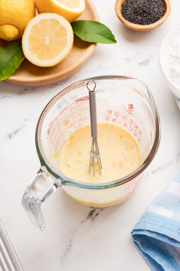 The wet ingredients for the lemon poppyseed donuts in a glass measuring cup.