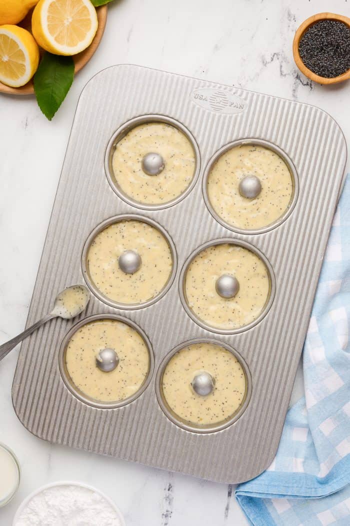 Unbaked lemon donuts in a metal donut baking pan.