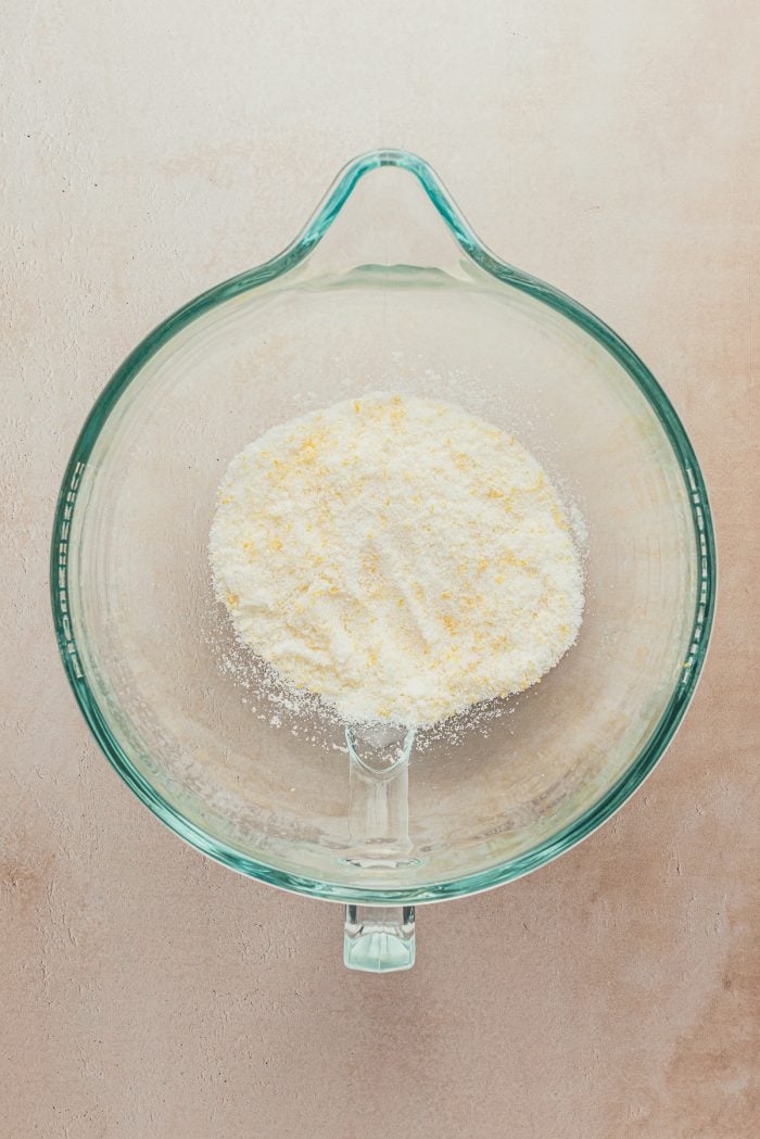 A glass bowl containing sugar with lemon zest.