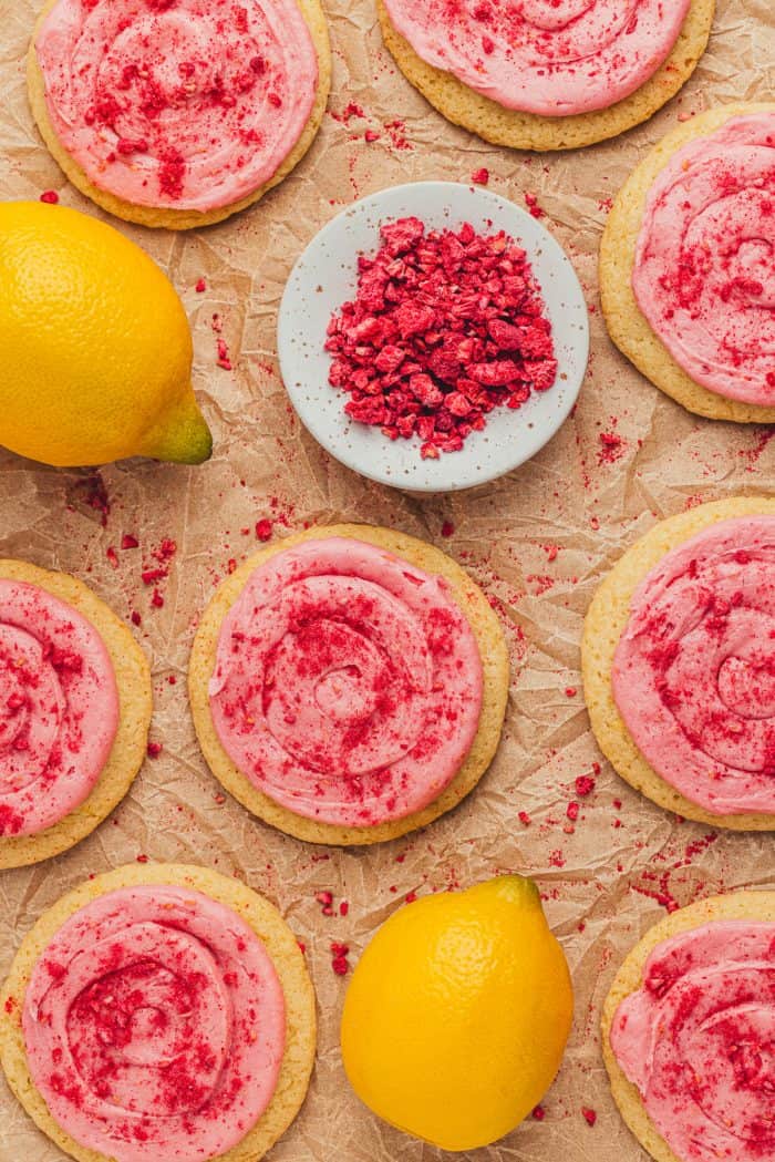 Lemon sugar cookies with raspberry cream cheese frosting on parchment paper.