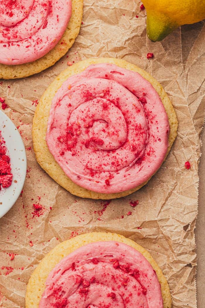 Lemon sugar cookies with raspberry cream cheese frosting on parchment paper.