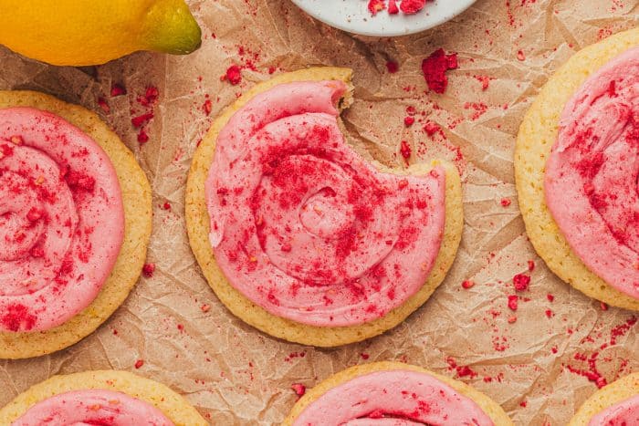 Lemon sugar cookies with raspberry cream cheese frosting on parchment paper.