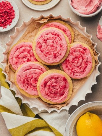 Lemon sugar cookies with raspberry cream cheese frosting in a white dish with lemons.