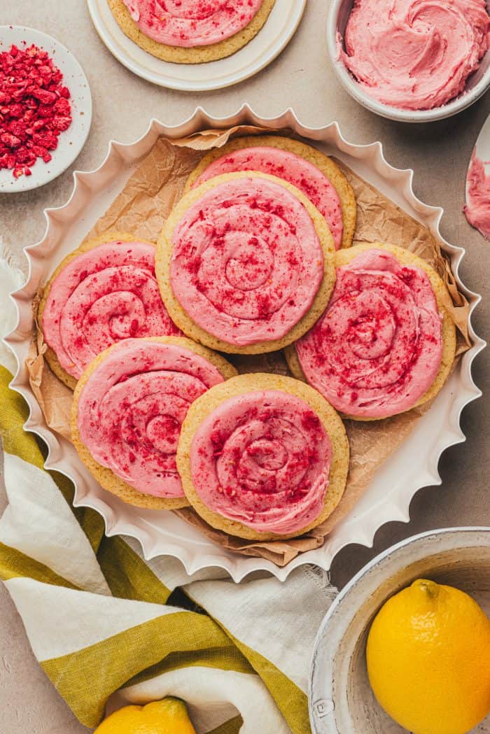 Lemon sugar cookies with raspberry cream cheese frosting in a white dish with lemons.