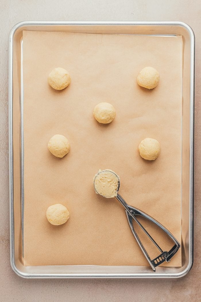 A cookie sheet with unbaked lemon sugar cookies on it and a cookie scoop with cookie dough.