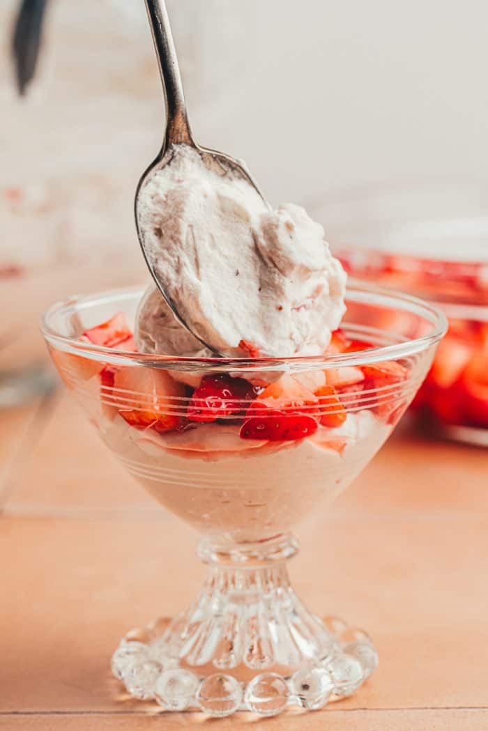 A layer of strawberry fool over fresh strawberries in a glass serving dish.