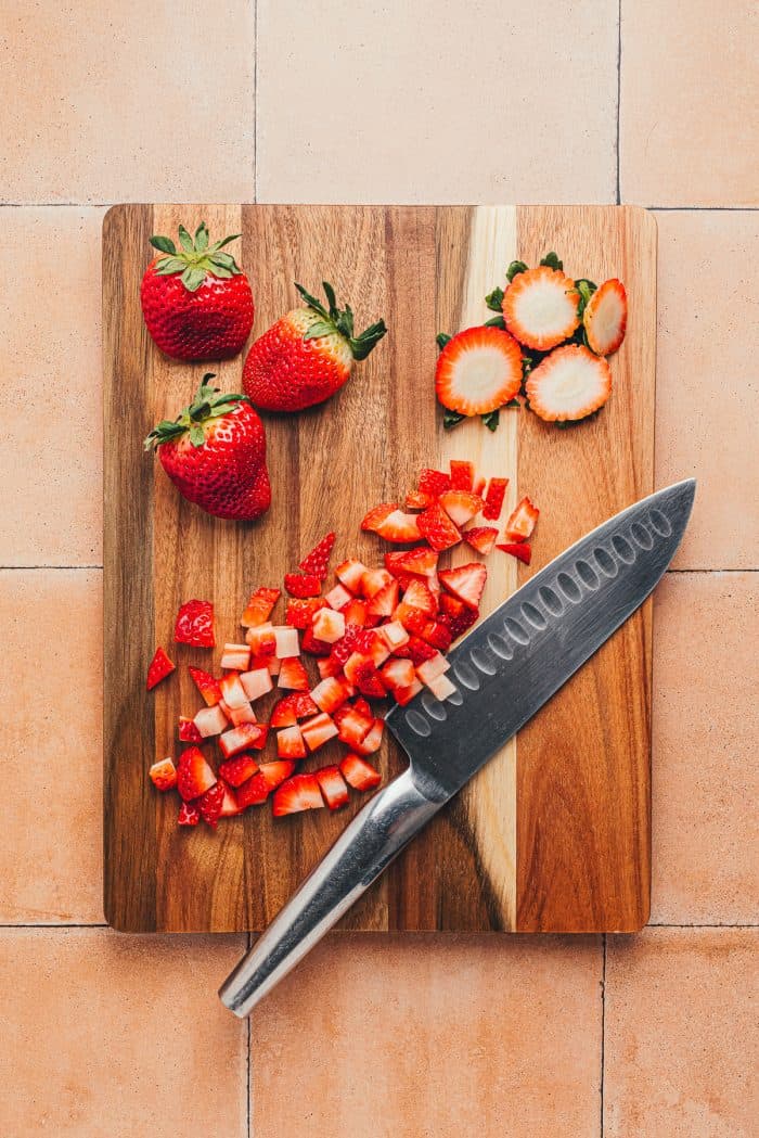 Diced strawberries with a knife on a wooden cutting board.