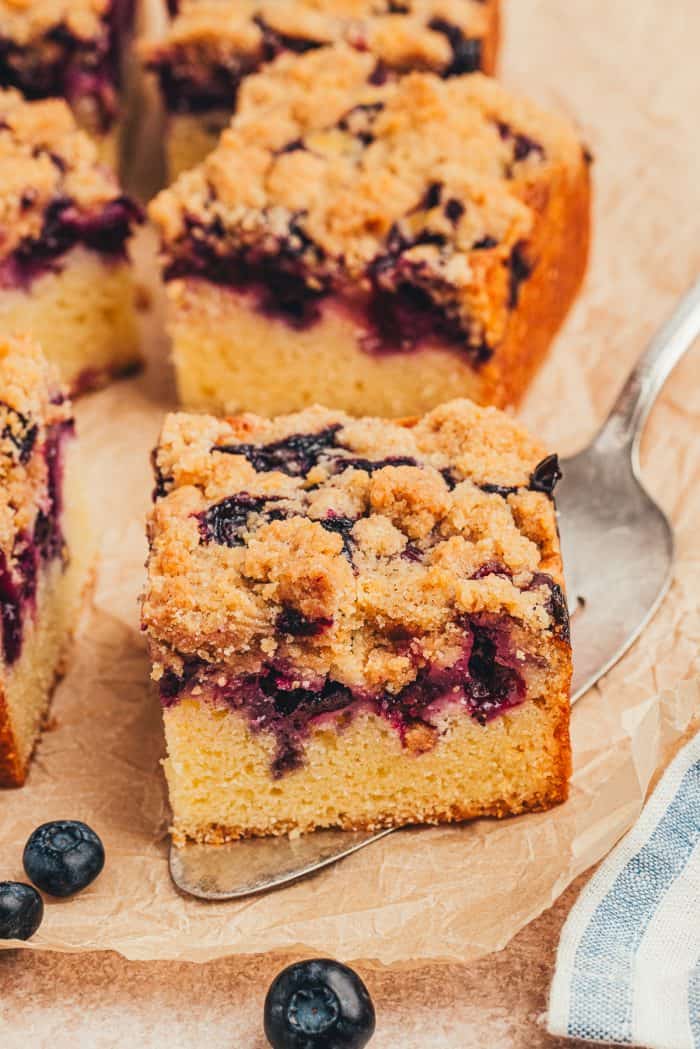 A slice of blueberry crumb cake on a cake slicer with slices behind it.