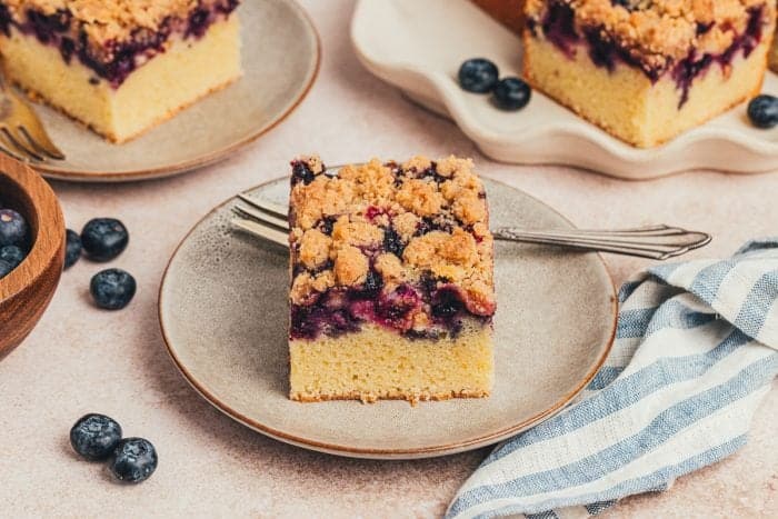 Three blueberry crumb cake slices on small plates. 