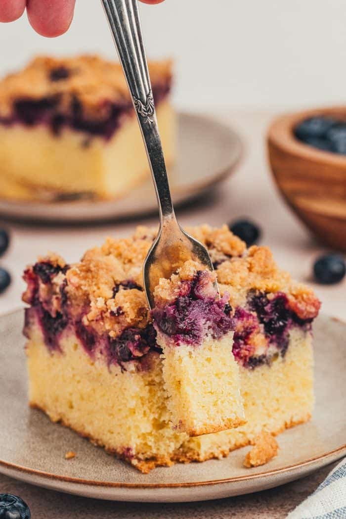 Blueberry crumb cake slice on a small plate with a fork taking a bite out of it.