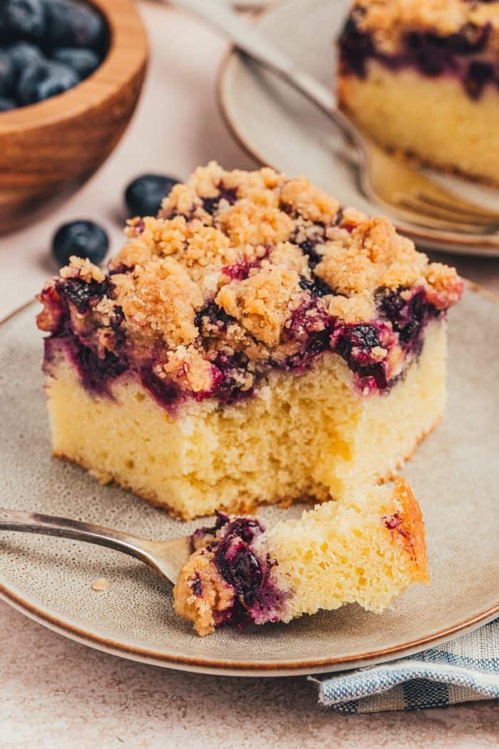 Blueberry crumb cake slice on a small plate with a fork taking a bite out of it.