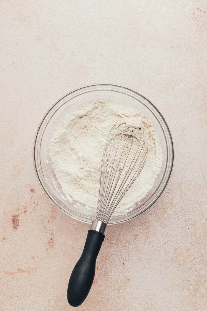 The dry ingredients in a glass bowl with a whisk.