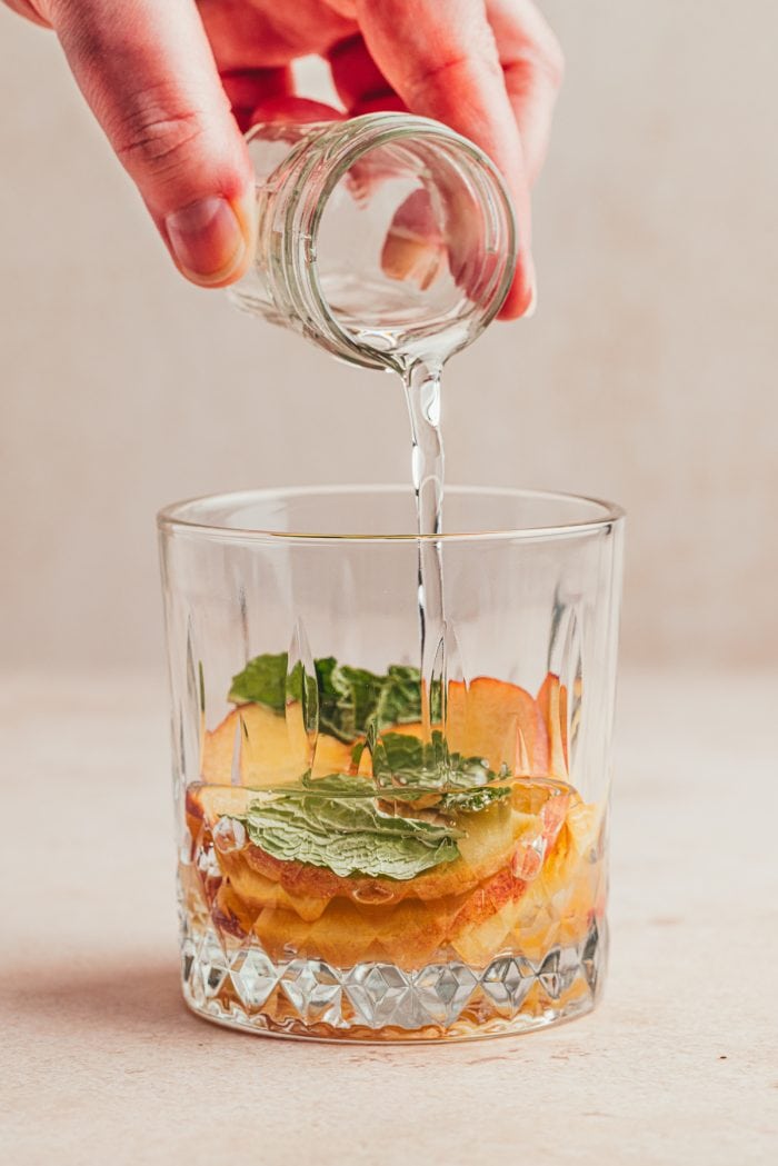 Peaches in a glass with simple syrup being poured in it.
