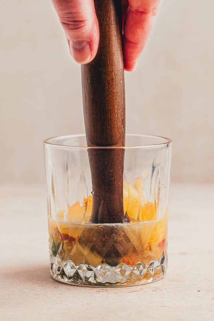 Peaches being muddled in a glass.