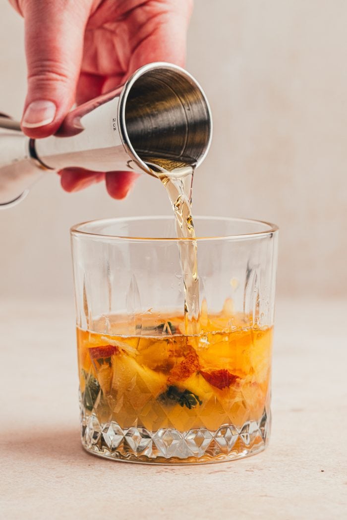 Bourbon being poured into a glass with sliced peaches.