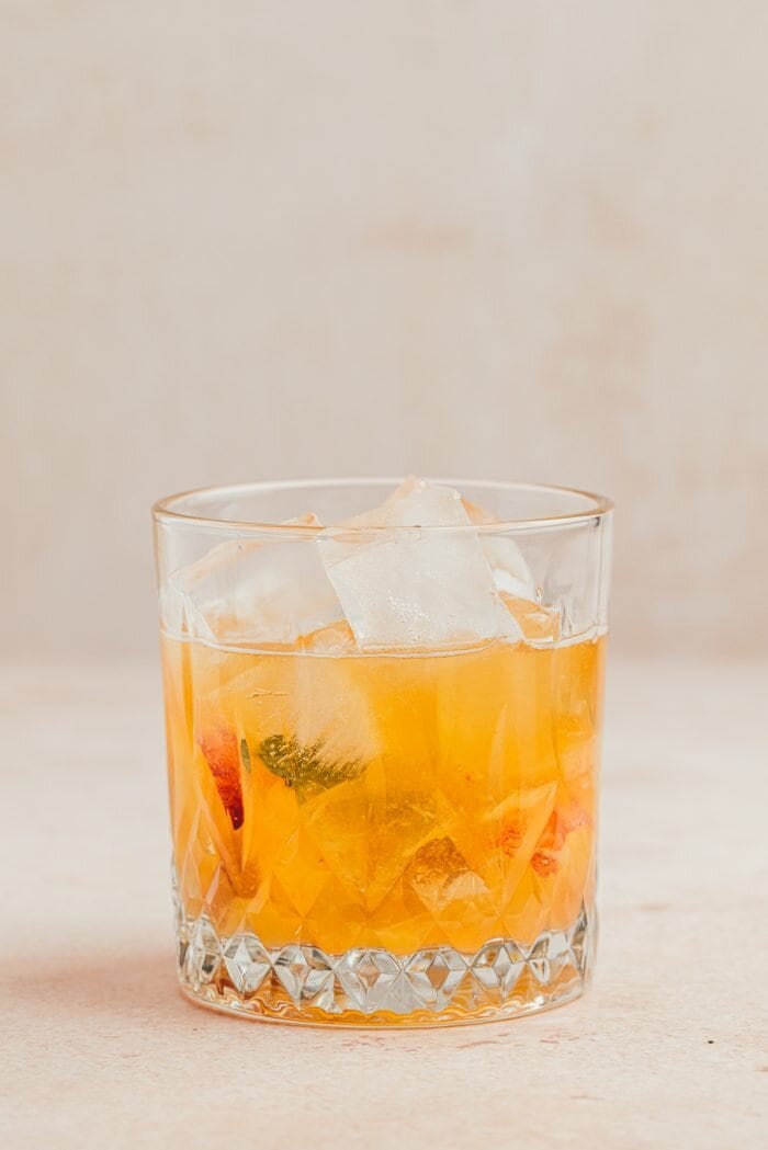 Ice being added to a glass of peach bourbon smash.