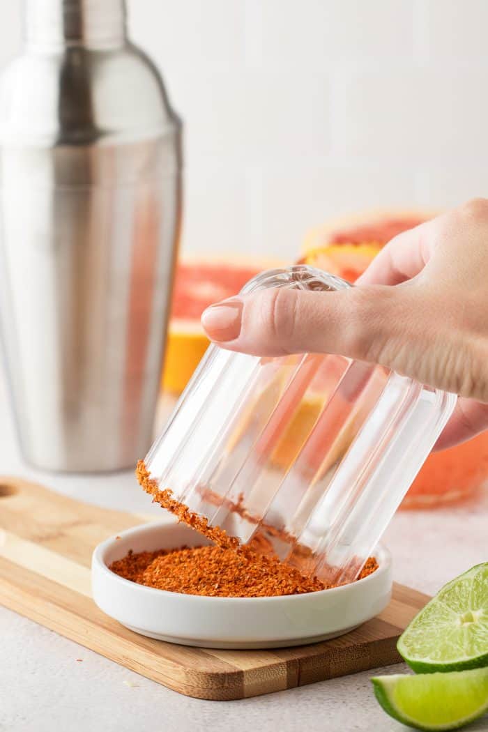 A cocktail glass being dipped into Tajin.