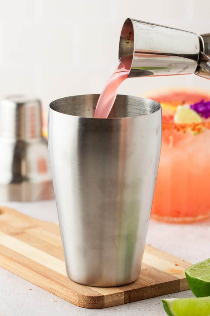 Filling a cocktail shaker with the drink mixture to make a Guava Paloma.