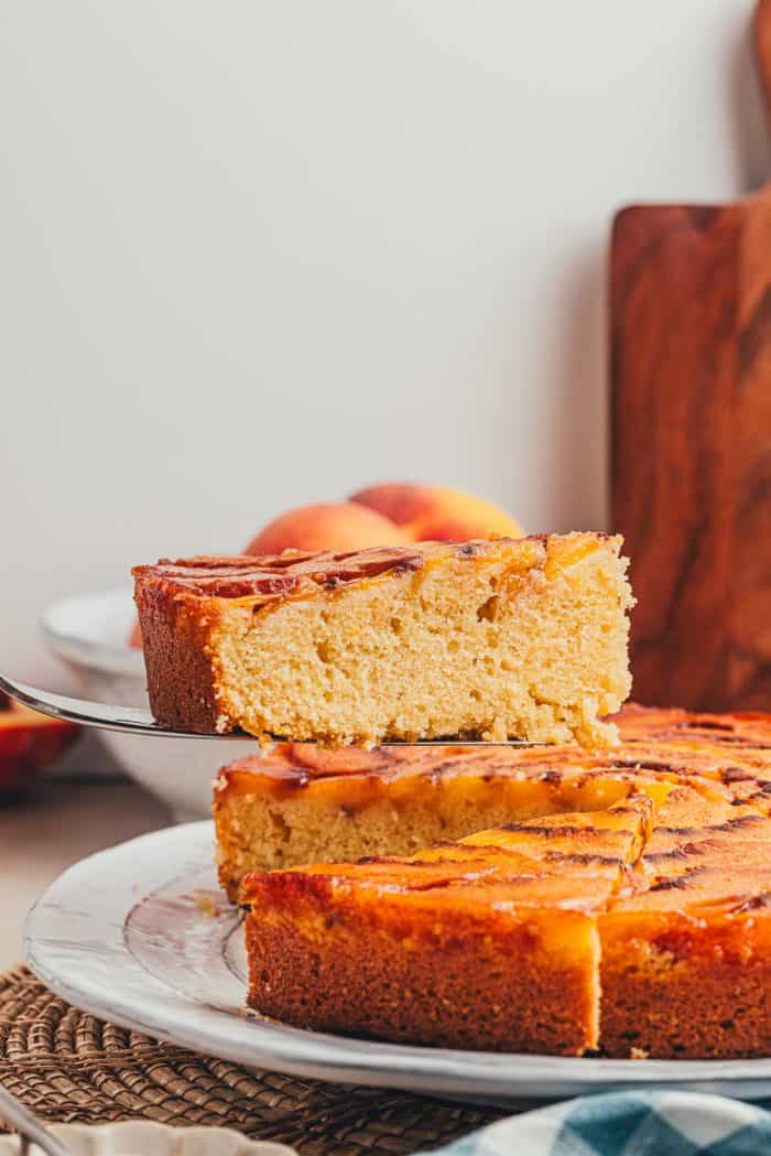 A slice of peach upside down cake being removed from the whole cake.