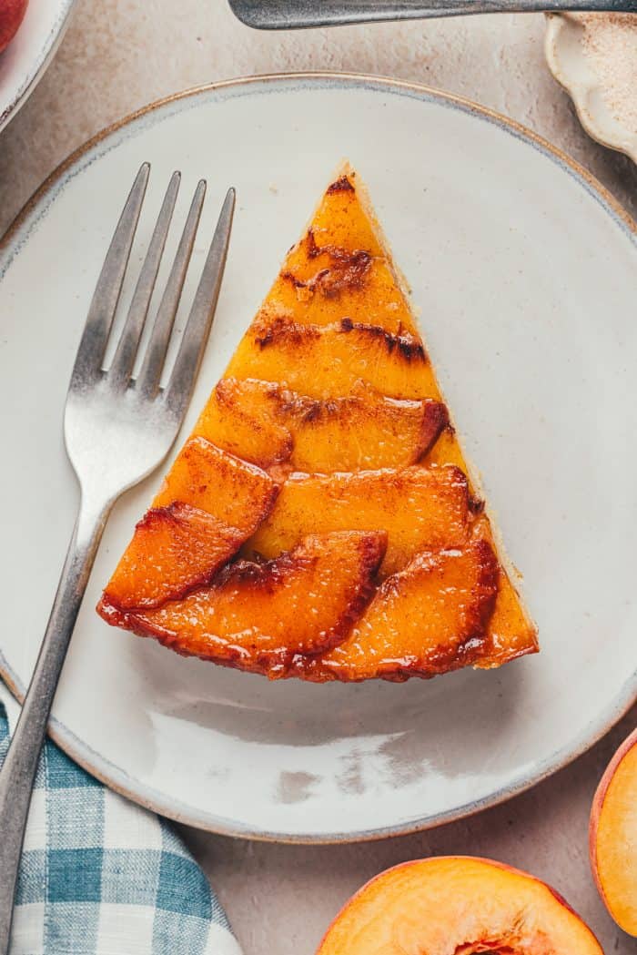 A slice of peach upside down cake on a white plate.