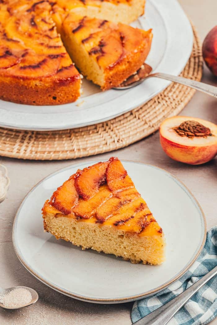A slice of peach upside down cake on a white plate.