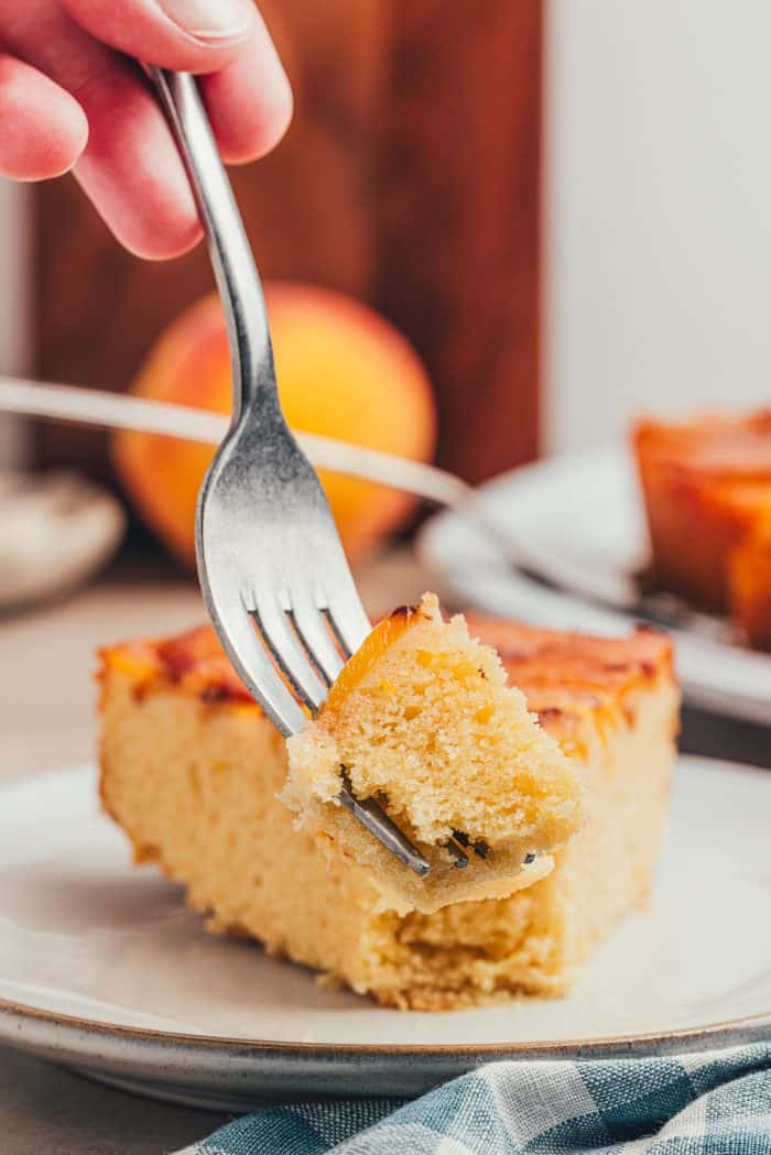 A slice of peach upside down cake on a white plate.