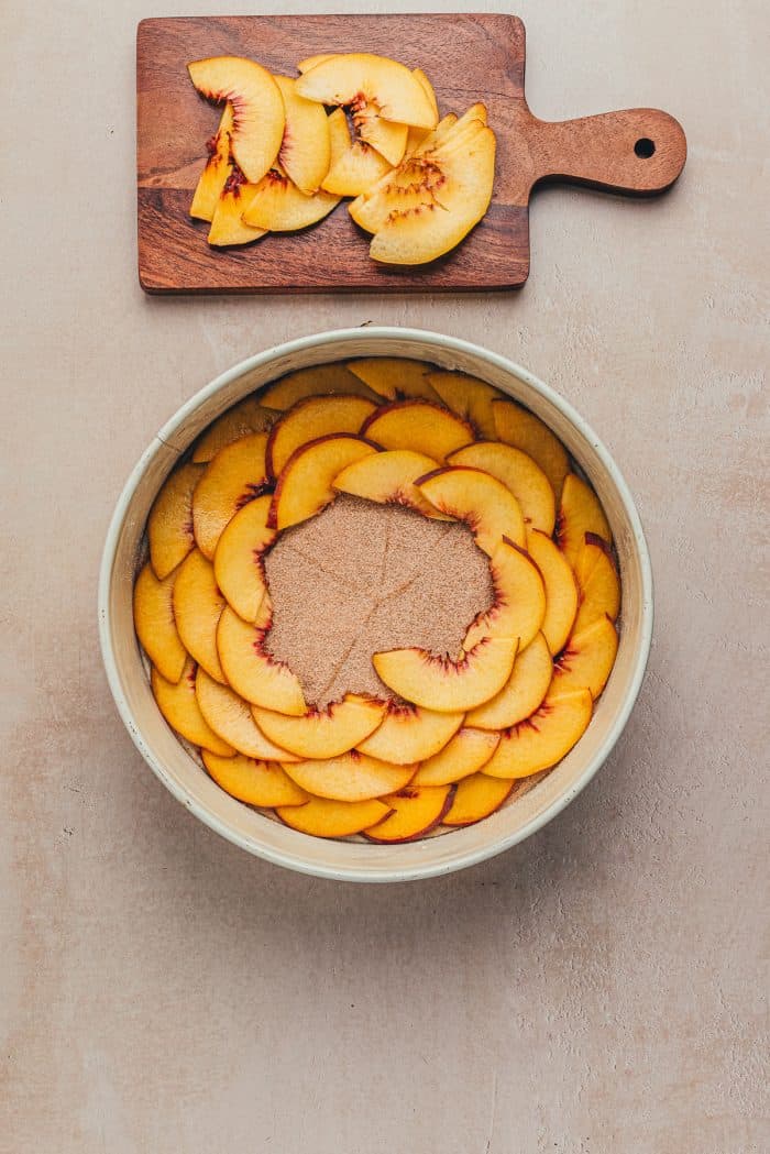 A round cake pan with sliced peaches on the bottom.