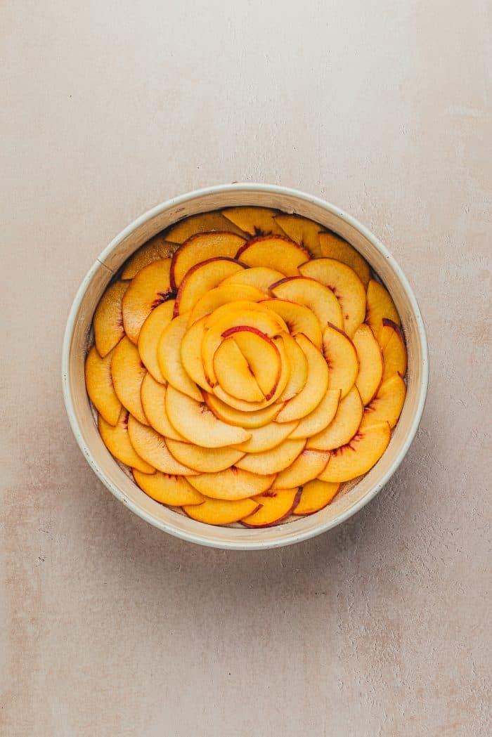 A round cake pan with sliced peaches on the bottom.