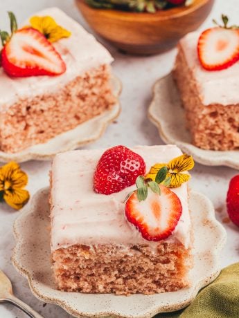 Three slices of strawberry sheet cake on plates with strawberries around them.